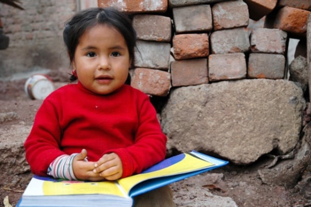 Niña pequeña sentada con un libro en la calle